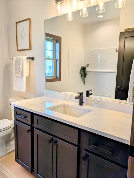 Bathroom vanity with a white quartz top with gold veining, dark cabinets, and black fixtures