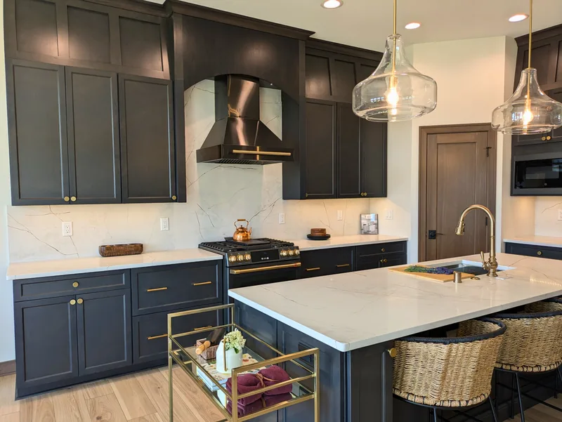 Showcase kitchen with dark cabinets, a white quartz island and full-height backsplash with soft gold veining, brass fixtures, and glass pendant lights